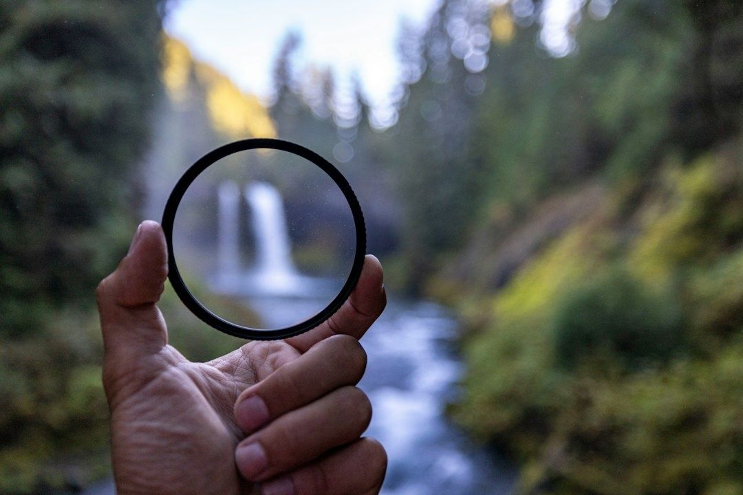 Hånd holder et rundt ND-filter foran en foss i skogen
